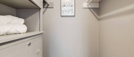A walk-in closet with a white dresser, a framed floral artwork on the wall, and a towel on the top shelf.