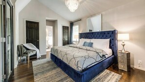 A bedroom with a large bed, a chandelier, a nightstand, and a chair. - Spacious 2-bedroom loft condo in Dallas’ Historic Munger Place featuring a private designer terrace, secure parking, luxury hybrid mattresses with Egyptian-cotton sheets, and a serene outdoor patio—perfect for relaxing or entertaining. (Dallas)