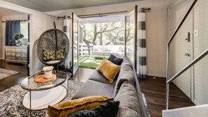 A modern living room with a sofa, a round chair, a glass coffee table, and a view of a garden through glass doors. - Spacious 2-bedroom loft condo in Dallas’ Historic Munger Place featuring a private designer terrace, secure parking, luxury hybrid mattresses with Egyptian-cotton sheets, and a serene outdoor patio—perfect for relaxing or entertaining. (Dallas)