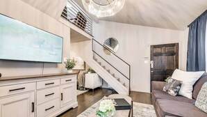 A modern living room with a flat-screen TV, a staircase, a sofa, and a coffee table. - Bright and airy 2BR/1BA loft in Dallas’ Historic Deep Ellum/Junius Heights District. Features king & queen beds, private balcony, and access to an offsite award-winning courtyard retreat. (Dallas)