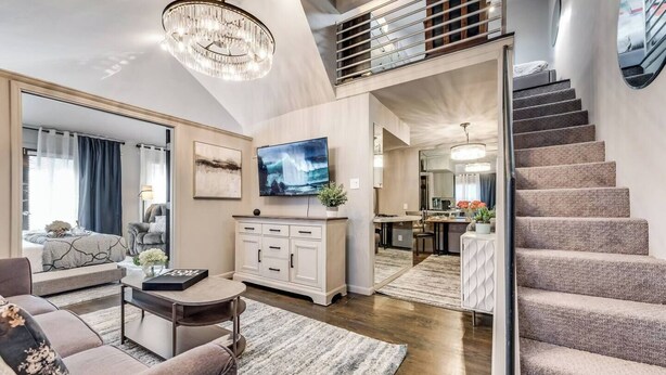A modern living room with a sofa, coffee table, TV, and a staircase leading to an upper level. - Bright and airy 2BR/1BA loft in Dallas’ Historic Deep Ellum/Junius Heights District. Features king & queen beds, private balcony, and access to an offsite award-winning courtyard retreat. (Dallas)