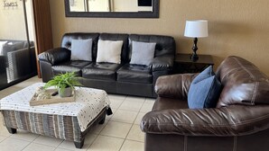 Ein Wohnzimmer mit einer schwarzen Ledersofa, einem kleinen Beistelltisch mit Lampe, einem Korbtisch mit Dekoration und einem großen Spiegel an der Wand.