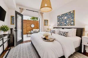 A modern bedroom with a large bed, a bedside table, a TV, and a view of the outdoors. - A bright one-bedroom condo with a clean, inviting interior and an easygoing atmosphere, just steps from the Santa Fe Trail and close to Munger Park. (Dallas)