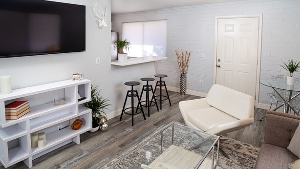 A modern living room with a flat-screen TV, white shelving, a white sofa, a glass coffee table, and a small bar area with stools. - Quaint Central Phoenix Duplex   (Phoenix)