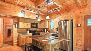A wooden cabin interior with a stone island, bar stools, a refrigerator, and a kitchen with wooden cabinets and a microwave.