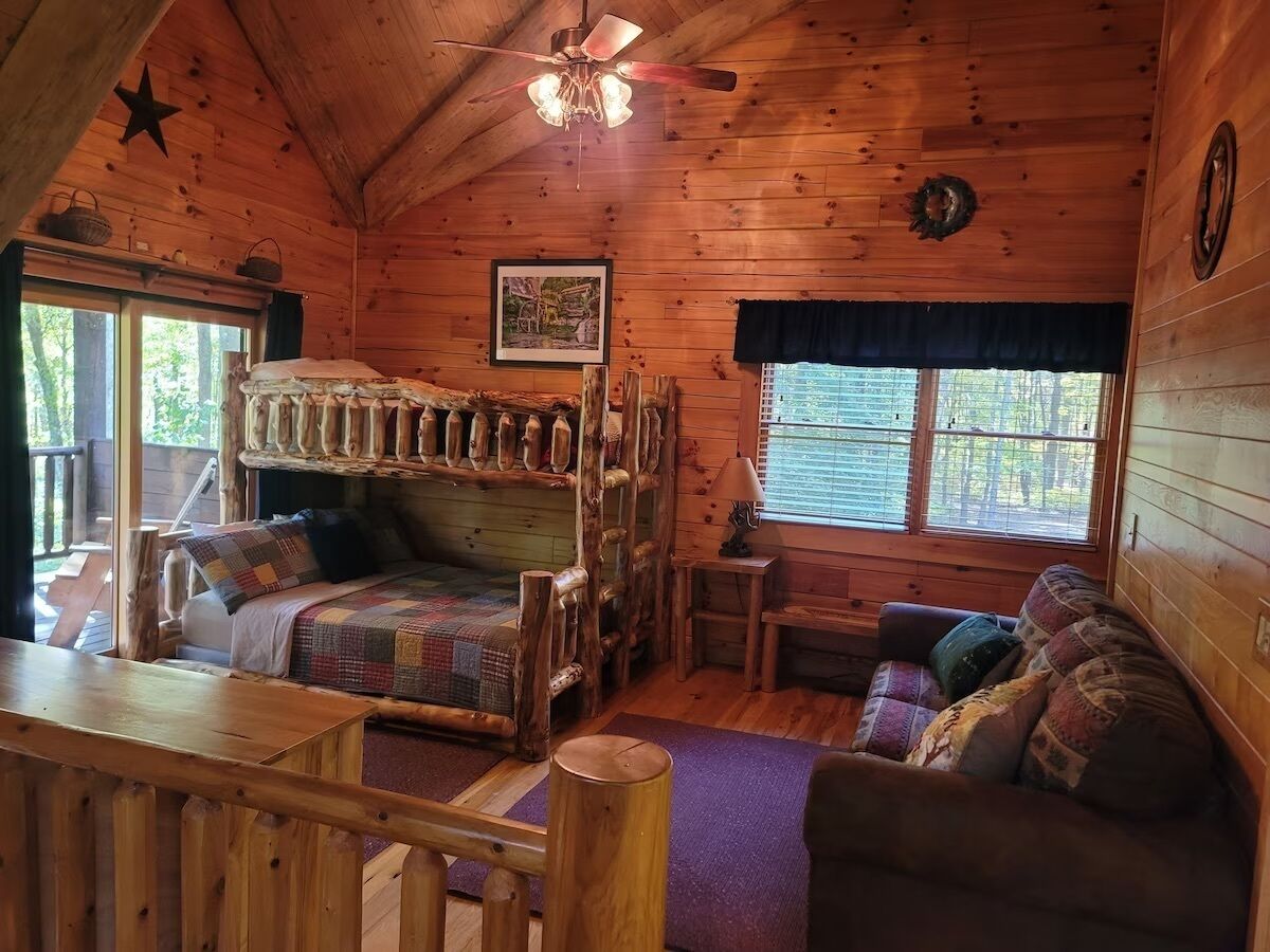 Un intérieur de chalet chaleureux avec un lit superposé, un canapé, une petite table et un ventilateur de plafond.