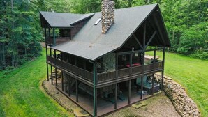 A two-story log cabin with a stone chimney, a balcony, and a stone wall surrounding the property.