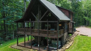 A cabin with a balcony, stone foundation, and a hot tub.