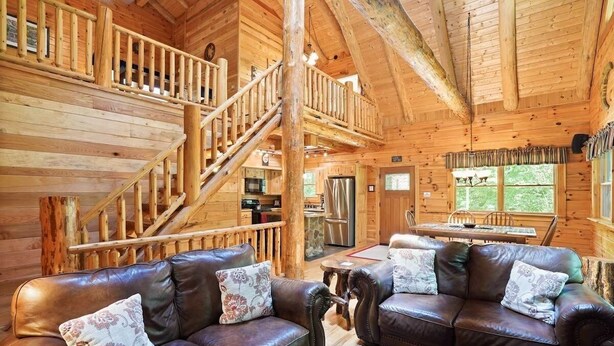 A wooden cabin interior with a staircase, leather sofas, a dining area, and a kitchen.