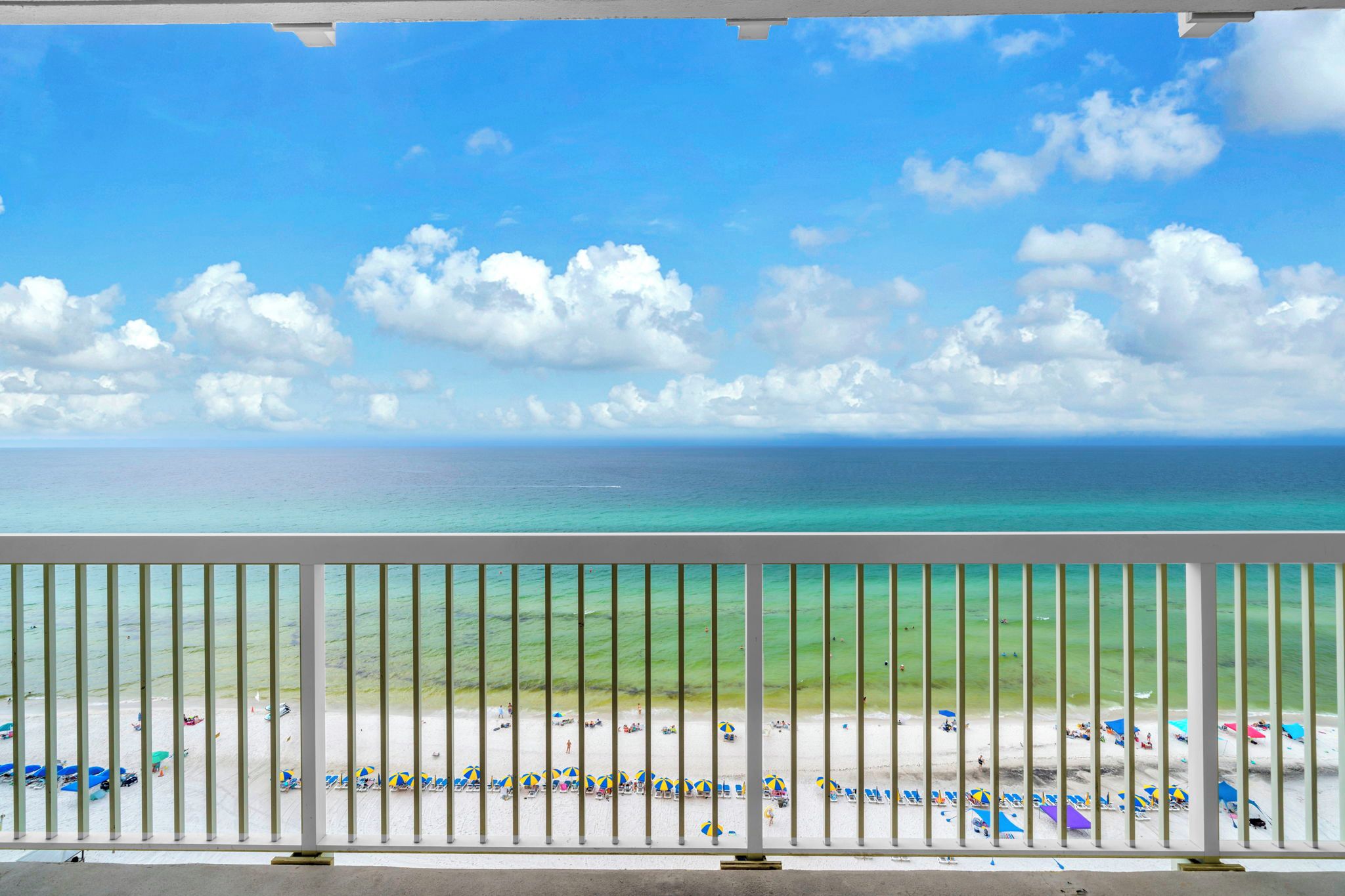 A balcony with a view of a beach, a railing, and a clear sky.