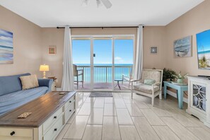 A room with a balcony, a sofa, a chair, a table, and a cabinet. - 🏖️Beach Front-FREE Beach Service-Pools-Celadon 1103🏖️ (Panama City)