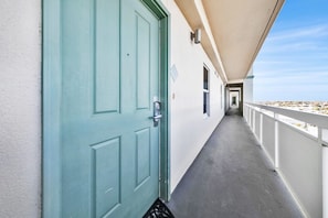 A corridor with a teal door, a security camera, and a balcony with a railing. - 🏖️Beach Front-FREE Beach Service-Pools-Celadon 1103🏖️ (Panama City)