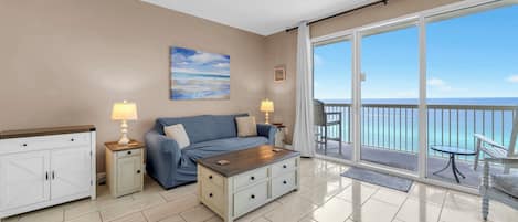 A room with a sofa, coffee table, and a view of the ocean through large glass doors.