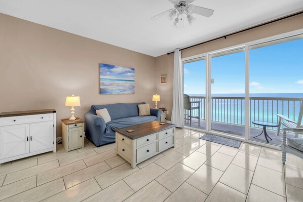 A room with a sofa, coffee table, and a view of the ocean through large glass doors.
