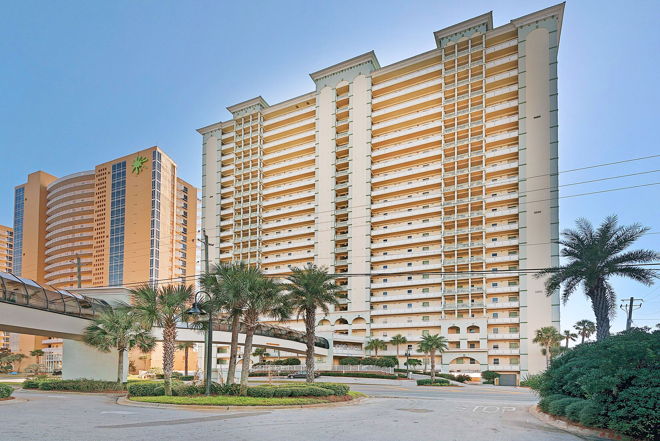 A high-rise hotel with multiple balconies, a covered walkway, and palm trees.