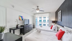 Ein modernes Hotelzimmer mit Bett, Schreibtisch, Fernseher und einem Balkon mit Blick auf Gebäude.