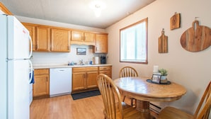 A kitchen with wooden cabinets, a white refrigerator, a dishwasher, a dining table with chairs, and a window with blinds. - 1BR I Downtown, Queen, Free W/D, Garage (Fargo)