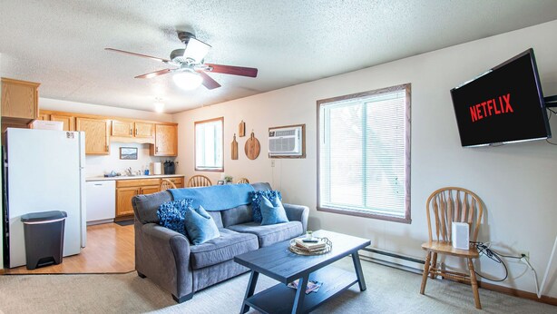 A living room with a sofa, coffee table, TV, and kitchen in the background. - 1BR I Downtown, Queen, Free W/D, Garage (Fargo)