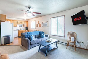 A living room with a sofa, coffee table, TV, and kitchen in the background.