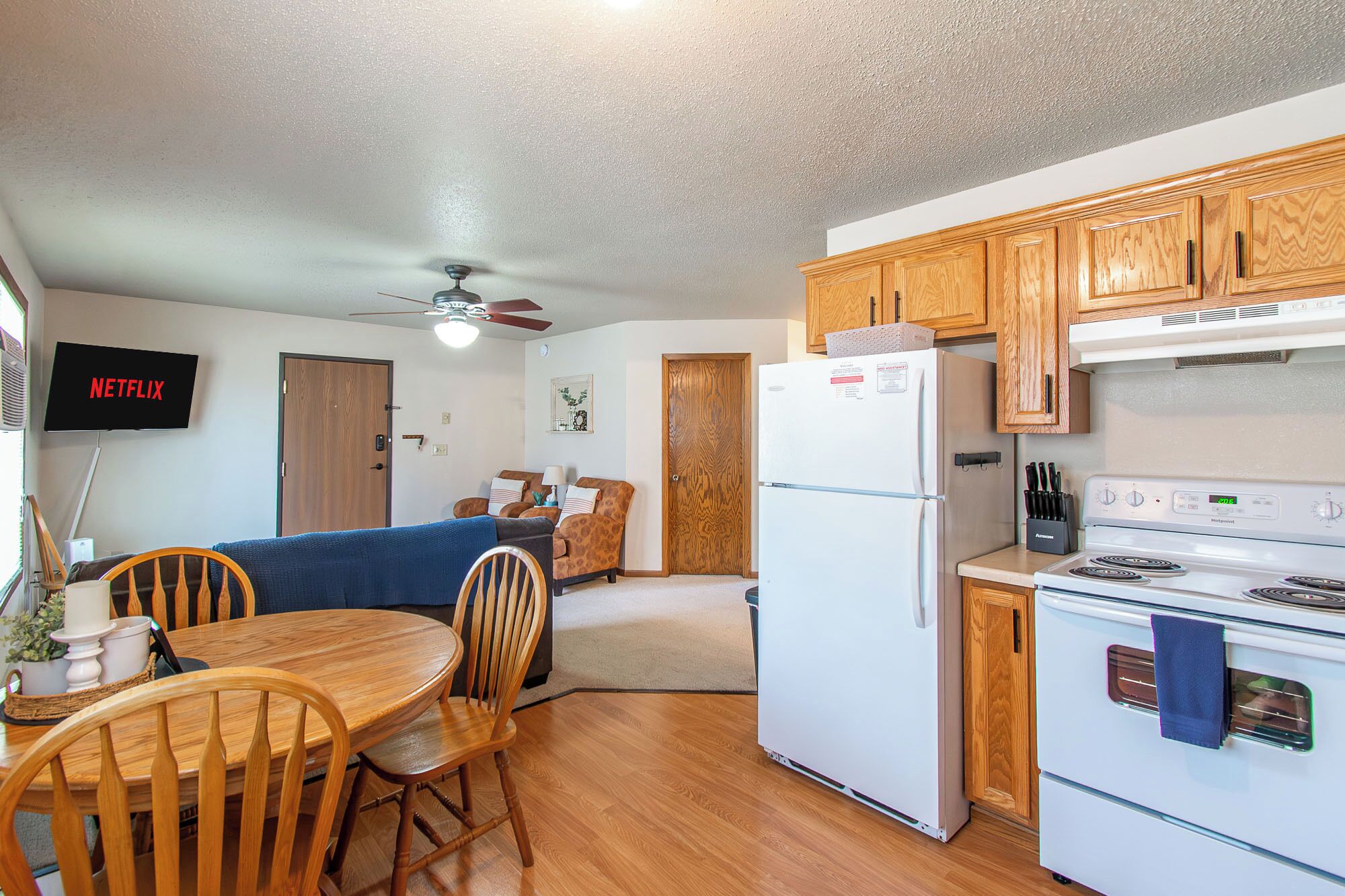 Una cocina compacta con armarios de madera, un refrigerador, una estufa y un comedor con mesa y sillas.