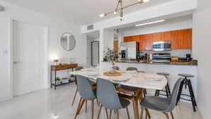 Una cucina moderna con elettrodomestici in acciaio inossidabile, mobili in legno e un'area pranzo con tavolo bianco e sedie grigie.