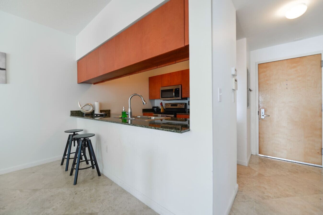 Una cocina compacta con microondas, horno y una pequeña barra con taburetes.