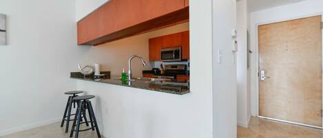Una cocina compacta con microondas, horno y una pequeña barra con taburetes.