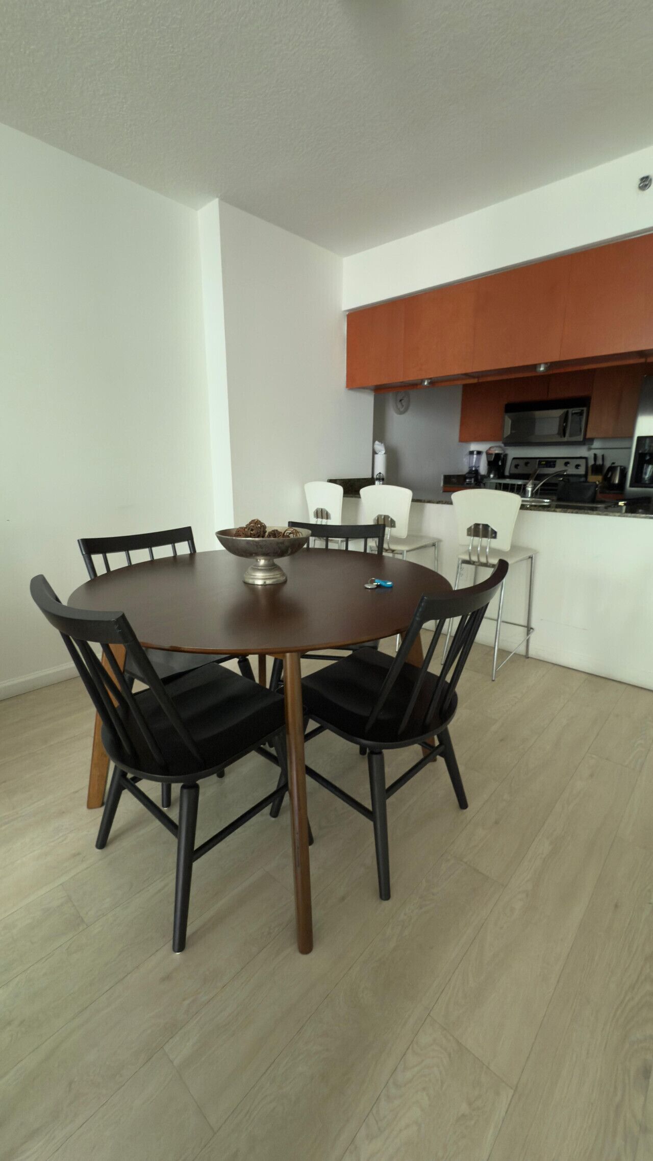 Un coin repas avec une table ronde et quatre chaises, une cuisine équipée d’un four à micro-ondes et d’une cuisinière, et un mur blanc.