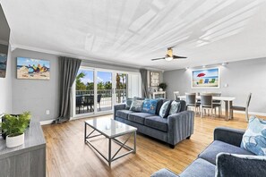 A modern living room with a grey sofa, a coffee table, and a dining area with a white table and chairs.