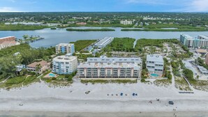 Vue aérienne d’un hôtel situé sur la côte, composé de plusieurs bâtiments, avec une plage et un port de plaisance.