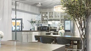 Eine moderne Küche mit Edelstahlgeräten, eine Essecke mit Holztisch und Stühlen sowie ein Zierbaum.