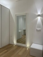 Una stanza con un ampio specchio, un armadio, un comodino e un punto luce a parete.