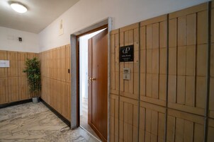 Corridoio di un hotel con pareti rivestite in legno, una pianta in vaso, una porta con la scritta 'Abba Rooms' e pavimento in marmo.