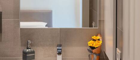 Ein Badezimmer mit Waschbecken, Spiegel, Seifenspender und einer Vase mit gelben Blumen.
