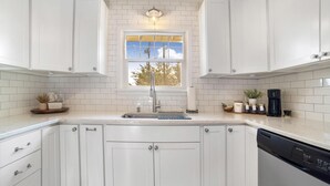 A kitchen with white cabinets, a window with a view, a sink, and a coffee maker.