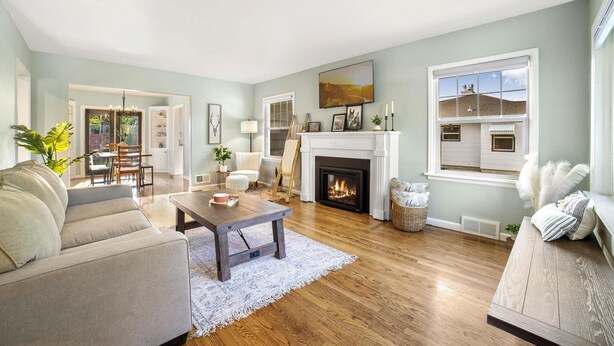 A living room with a fireplace, a sofa, a coffee table, and a dining area visible through an open door.