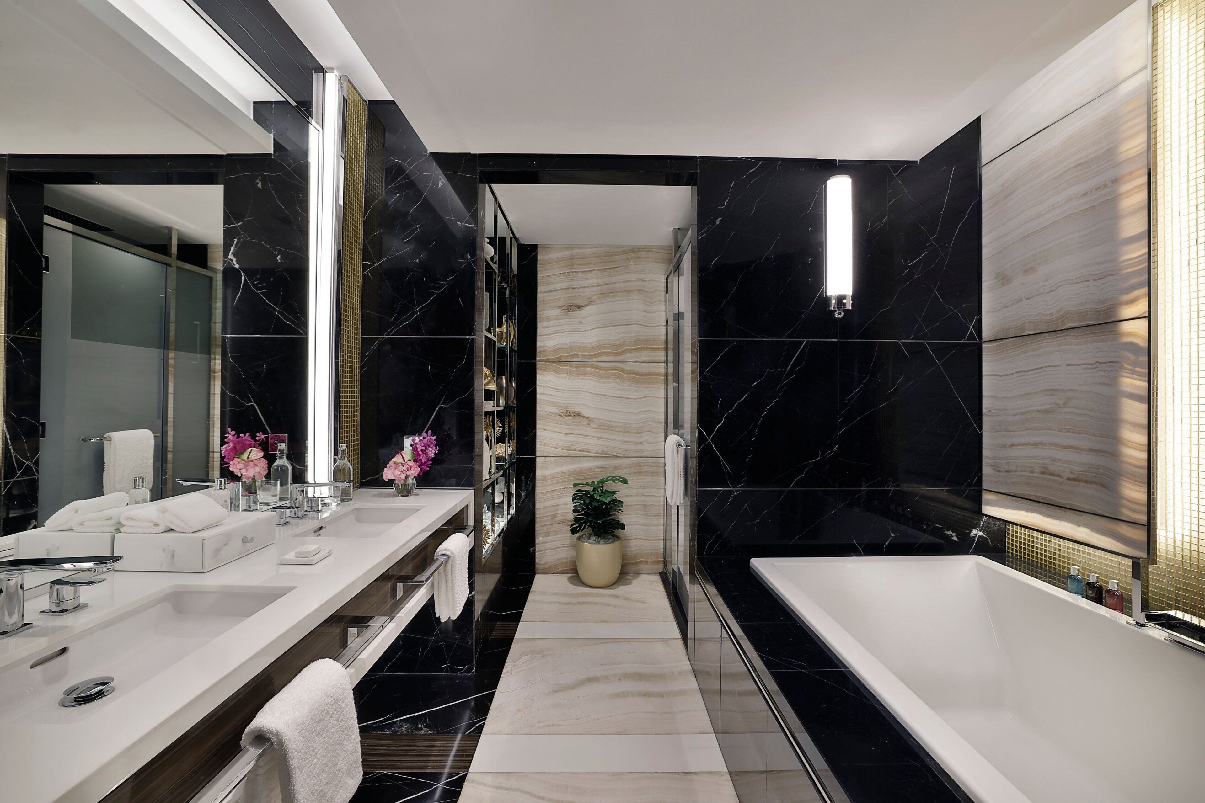 Un baño moderno con un espejo grande, dos lavamanos, una bañera y una planta en maceta.