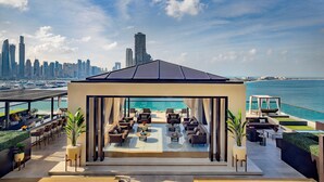 A rooftop lounge with a city skyline view, outdoor seating, and a poolside area.