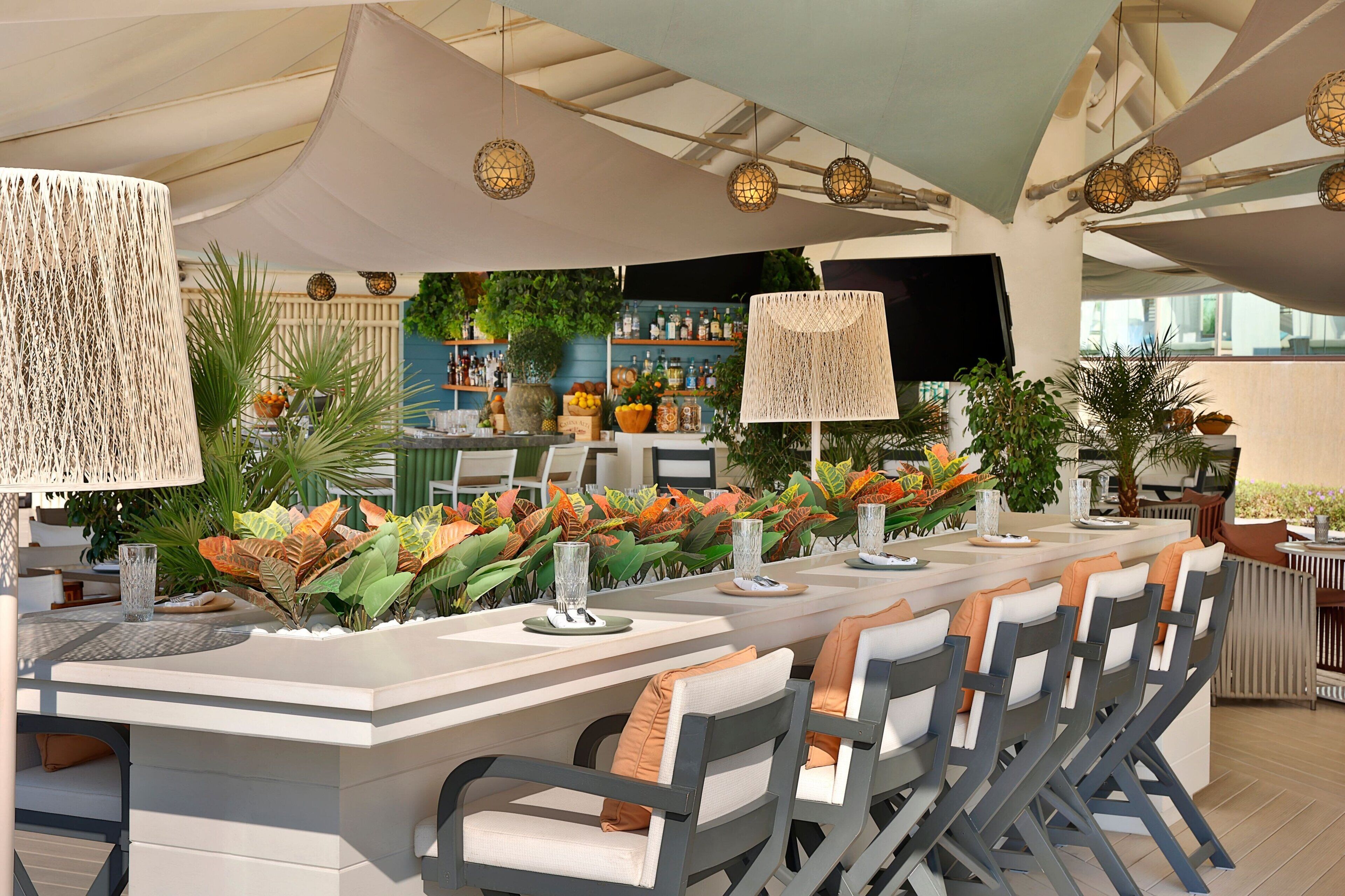 An outdoor dining area with a long white table, grey chairs, and decorative lamps.
