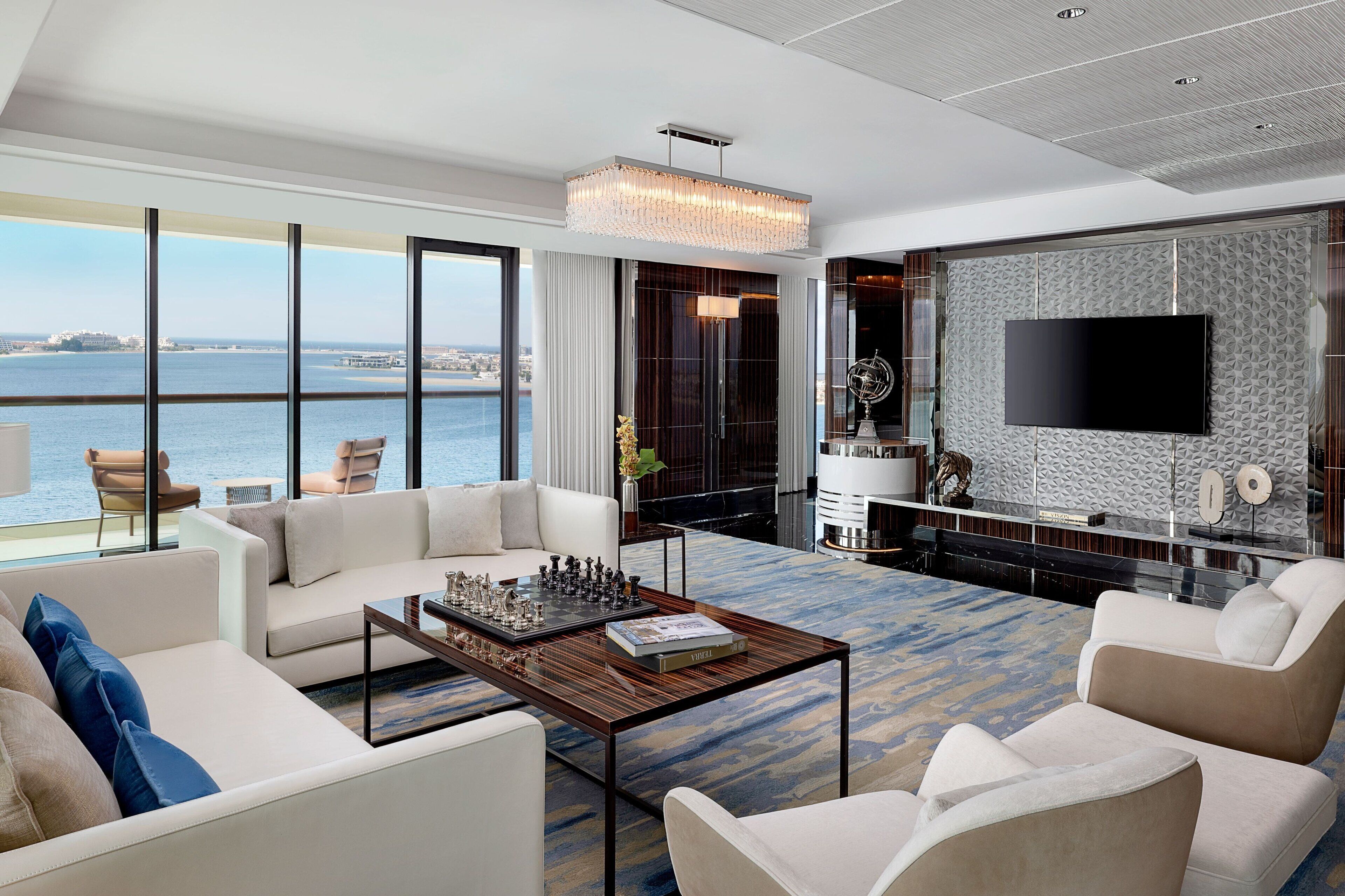 Una sala de estar moderna con un televisor grande, asientos cómodos, un tablero de ajedrez y vista al mar.