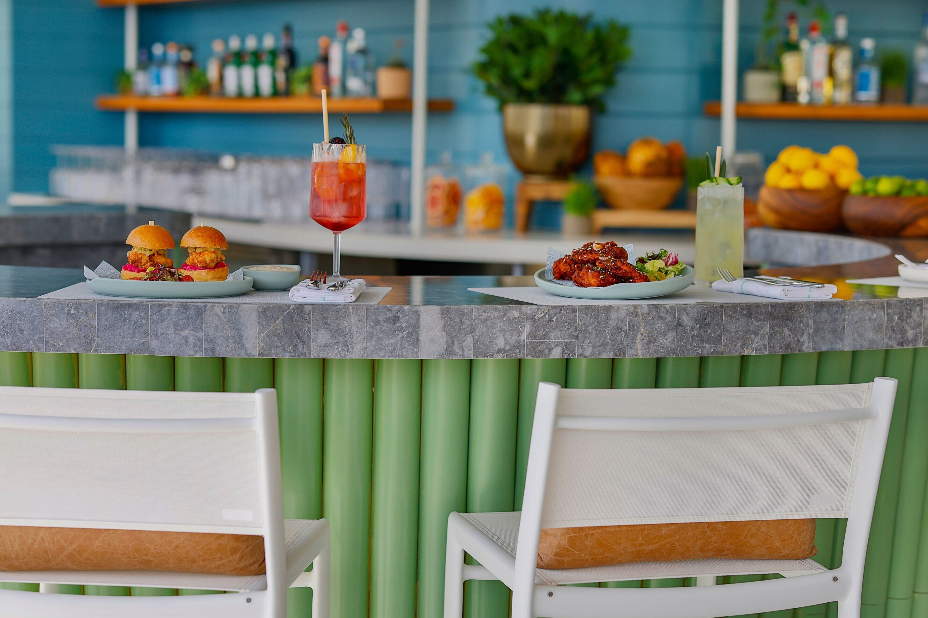 A bar area with a counter, two burgers, a salad, and two drinks.