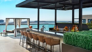 A rooftop bar with a view of the sea, featuring bar stools, a seating area, and a pergola.