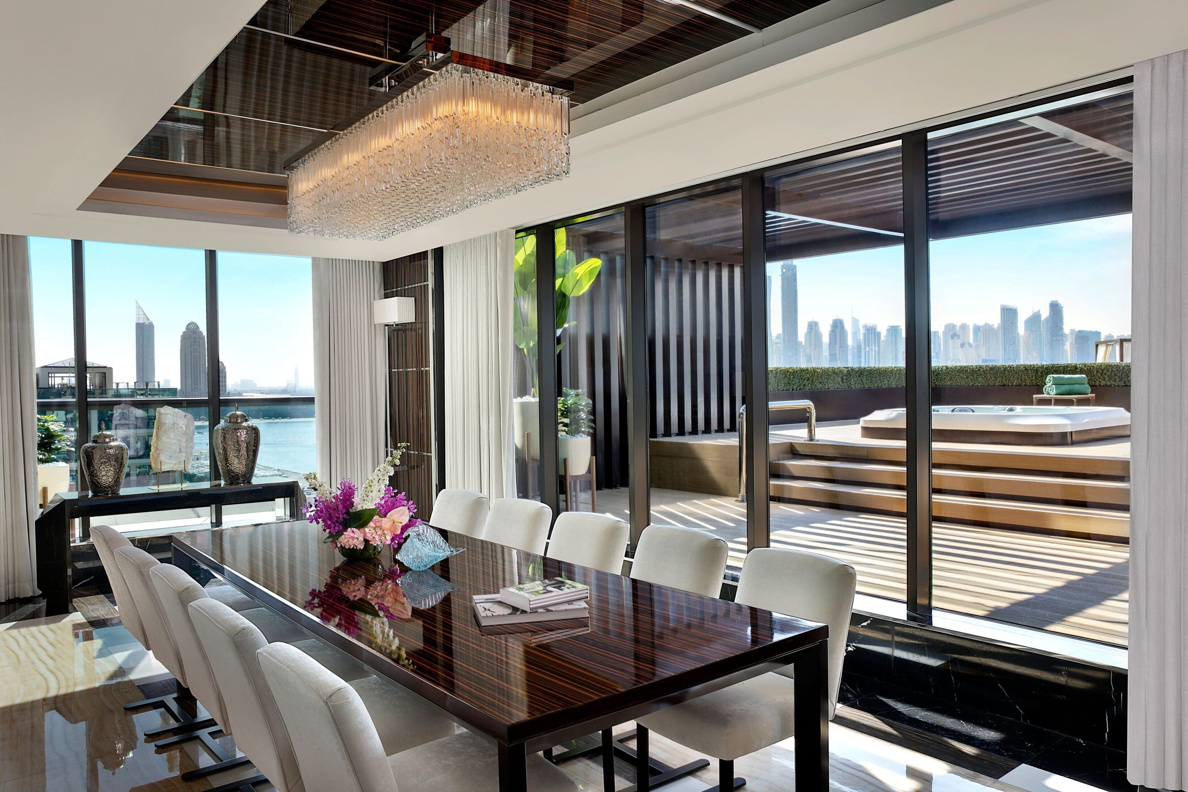 A modern dining area with a large table, white chairs, and a chandelier.