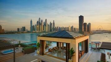 A modern rooftop lounge with a glass enclosure, offering a view of a city skyline and a body of water.