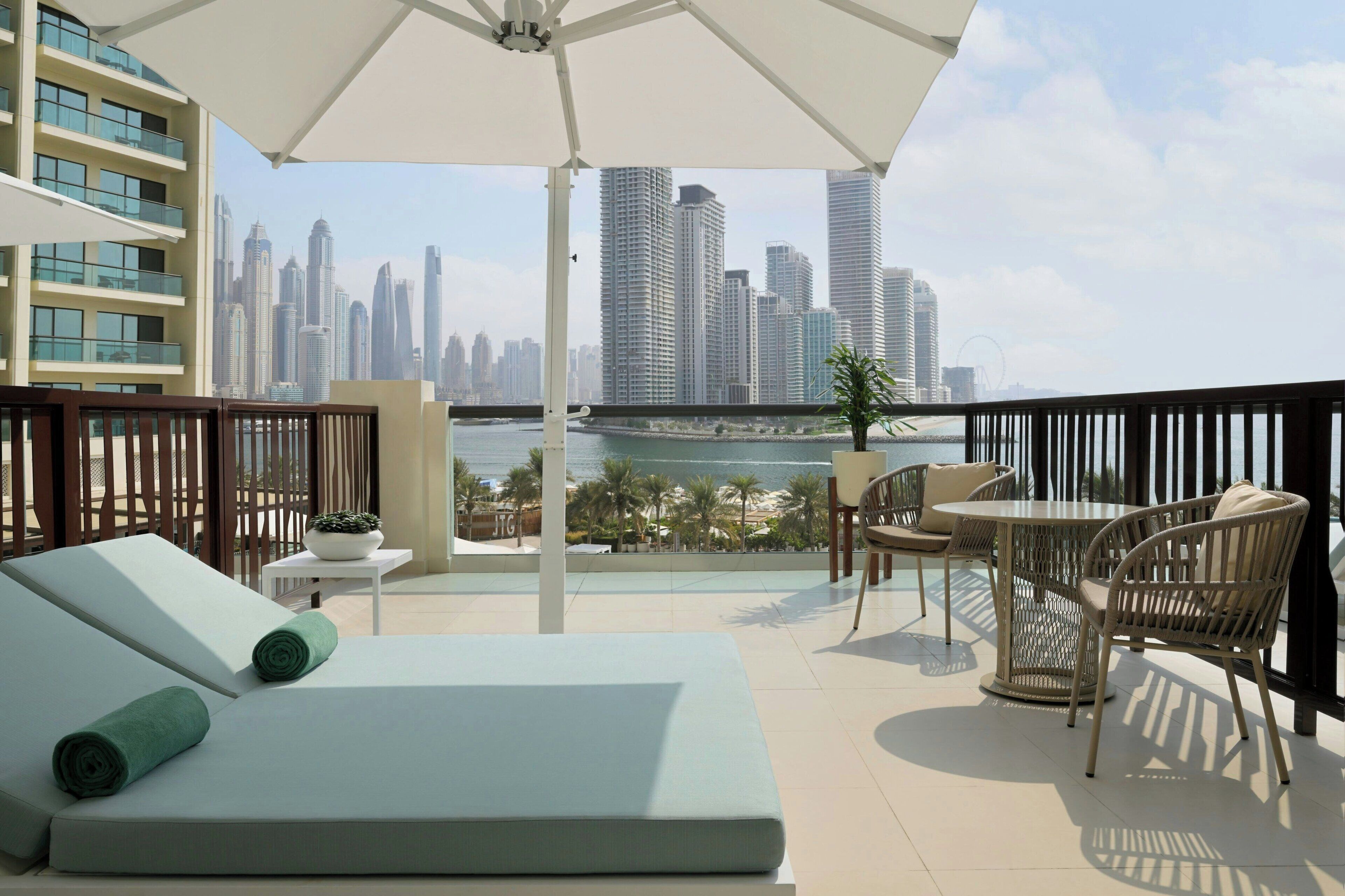 A balcony with a city view, a lounge area with a sofa and chairs, and a table with a potted plant.