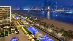 A hotel with a pool, palm trees, and a city skyline in the background.