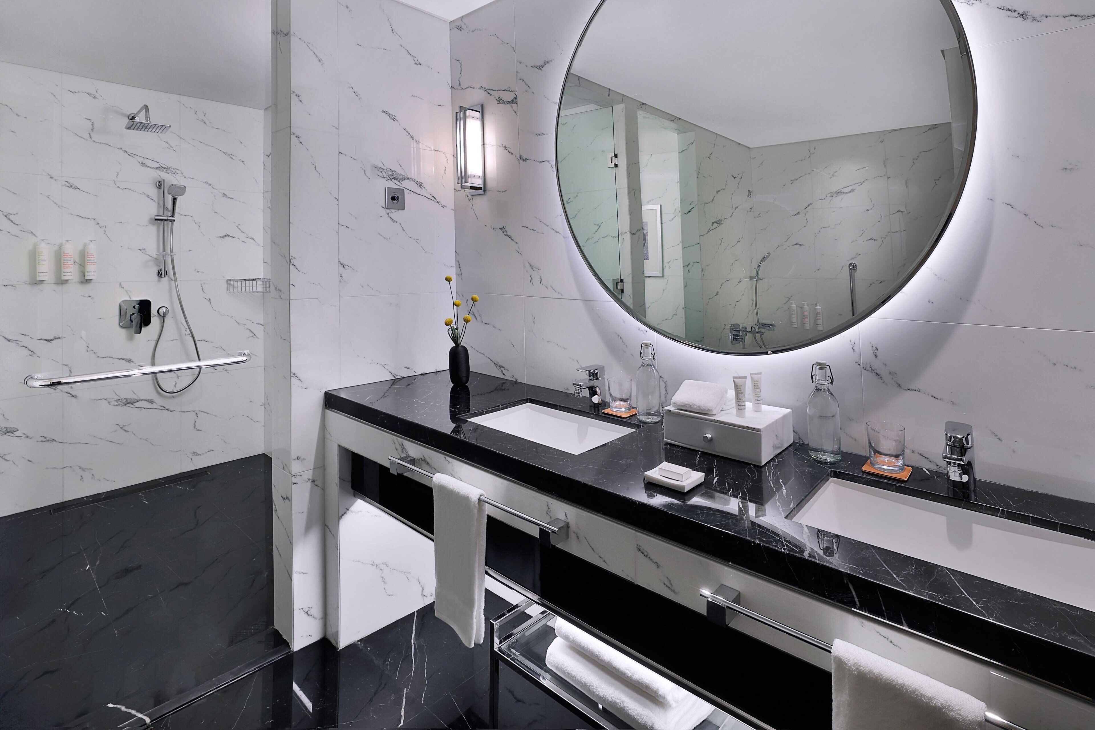 A modern bathroom with two sinks, a large mirror, and a shower.