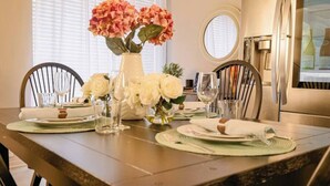 A dining area with a table set for four, a vase with flowers, and a refrigerator in the background.