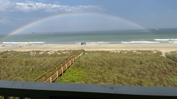A beach with a wooden boardwalk leading to the shore, a clear sky, and a rainbow.