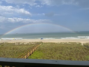 Una playa con un paseo marítimo de madera que conduce a la orilla, un cielo despejado y un arcoíris.